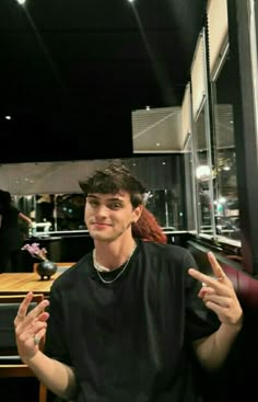 a young man sitting at a table with his hands in the air while talking to someone