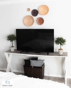 a flat screen tv sitting on top of a white table next to a basket filled with plants