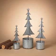 three metal christmas trees sitting next to each other on top of a wooden table with logs