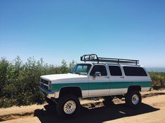 a white and green truck parked on top of a dirt road next to the ocean