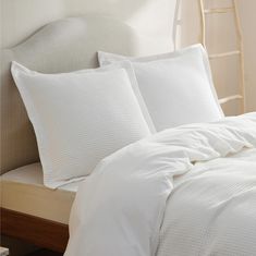 a bed with white sheets and pillows on it