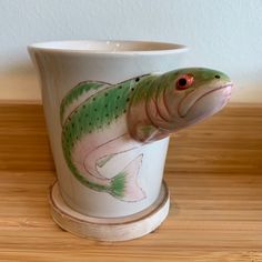 a green and pink fish on a white cup sitting on top of a wooden table