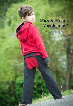 a young boy in red shirt and black pants standing on the road with his hands behind his back