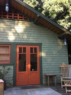 an orange door is on the side of a green building with two chairs and a bench