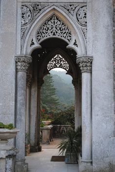 an archway leading into a garden with potted plants on either side and mountains in the background