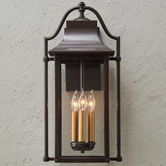 three candles are lit in an old fashioned lantern style light fixture against a white wall