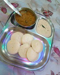 some food is sitting on a metal tray with sauce and spoons next to it