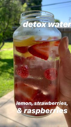 a person holding up a mason jar filled with lemon, strawberries and raspberries