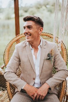 a man sitting in a wicker chair wearing a tan suit and flower boutonnier