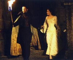 a man and woman dressed in period costumes holding hands while standing on steps with torches