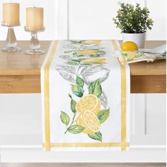 a table runner with lemons and leaves on it, next to two lit candles