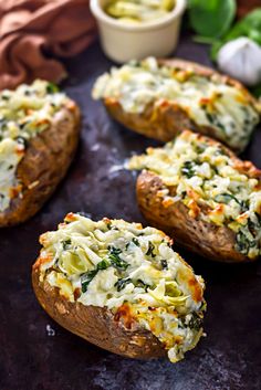 baked potatoes with spinach and cheese on a black surface next to some green leaves