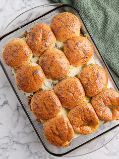 a pan filled with rolls covered in cheese on top of a marble counter next to a green towel