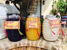 three large plastic containers sitting on top of a brick wall next to a tree and chairs