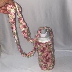 a hand holding a pink and white crocheted water bottle with a chain around it