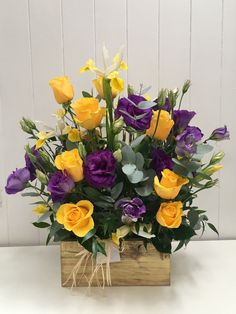 a bouquet of yellow and purple flowers sitting in a wooden box on a white table