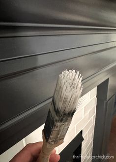 a person holding a paintbrush in front of a fire place with black painted fireplace mantels