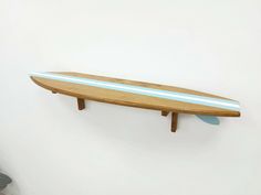 a surfboard mounted to the side of a white wall next to a wooden shelf