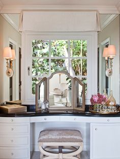 a white vanity with a mirror and stool in front of the window that is open