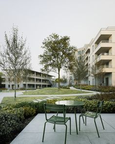 two green chairs sitting on top of a cement floor next to a lush green park