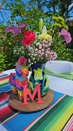 colorful flowers in a vase with the letter m on a wooden stand at an outdoor table