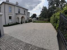 a large white house sitting next to a lush green park on top of a cobblestone road