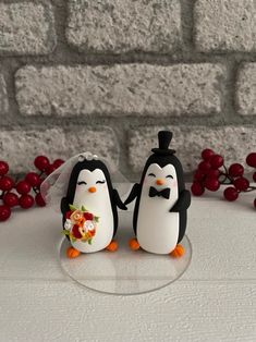 two penguins are standing next to each other in front of a brick wall and red berries