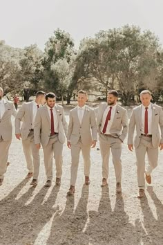 a group of men in suits standing next to each other on a dirt ground with trees in the background