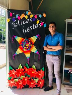 a man standing next to a sign that says felices fiestas with colorful ribbons