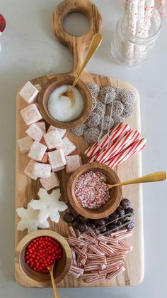 a wooden cutting board topped with candy canes, marshmallows and candies