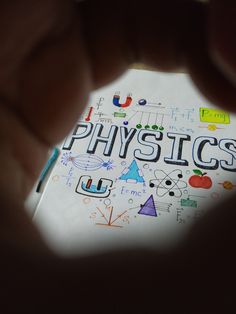 a person holding a piece of paper with the word physics written on it in front of them