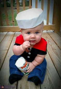 a baby wearing a chef's hat sitting on a wooden floor holding a can