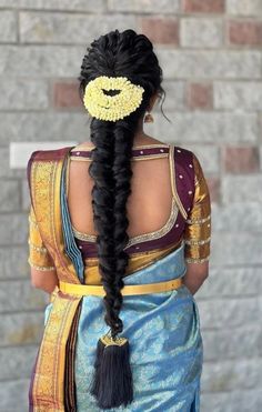 a woman with long black hair wearing a blue and yellow sari, braided into a