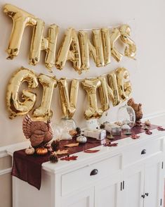 a table topped with gold foil balloons and thanksgiving decorations next to a sign that says thank you