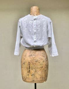 * Edwardian blouse c 1910s * White cotton * White hand-embroidered long-stemmed daisies and scalloped neckline and sleeve hem * 3/4 length set-in sleeves * Gathered into waistband both front and back * 8 button center back closure plus 2 hooks and eyes on waistband strap * Finished with French seams throughout No label Very good condition. There is a pinhole in front as shown in last image and some fraying on waistband's bottom edge. A lovely, wearable blouse. Bust: 34 Shoulder: 14 Sleeve: 14 Le Classic Floral Embroidered Tops For Daywear, Traditional Fitted Blouse For Daywear, Fitted Traditional Blouse For Daywear, Fitted Vintage Tops With Floral Embroidery, Vintage Blouse With Floral Embroidery For Daywear, Vintage Spring Blouse With Chikankari Embroidery, Vintage Cotton Blouse With Chikankari Embroidery, Vintage Blouse With Chikankari Embroidery For Spring, Vintage Chikankari Embroidery Blouse For Spring