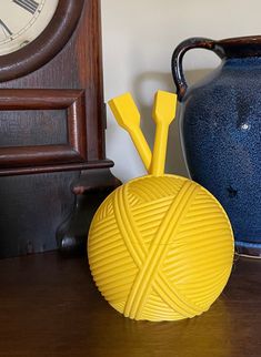 a blue vase sitting on top of a wooden table next to a yellow yarn ball