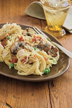 a plate of pasta with mushrooms and peas on it next to a glass of water