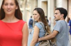 two people walking down the street with one woman looking at her phone and another man standing behind them