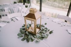 a lantern on top of a table surrounded by greenery and place settings for an event