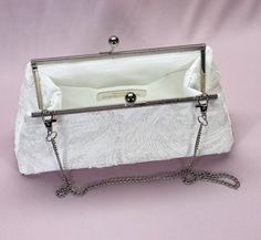 a white clutch bag with chain handles and an envelope on the front, sitting on a pink background