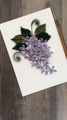 a white card with purple flowers and green leaves on it next to a wooden stick