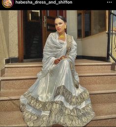 a woman sitting on some steps wearing a white and gold dress with her hand in her pockets