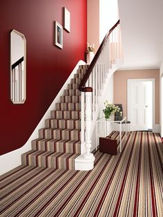 a hallway with red walls and striped carpet on the floor, along with white stairs