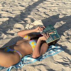 a woman laying in the sand with a book