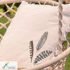 an embroidered pillow with feathers on it sitting in a hammock chair next to a plant