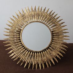 a mirror that is sitting on top of a brown cloth covered surface with gold spiky decorations