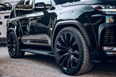 the front end of a black suv parked in a parking lot next to a building