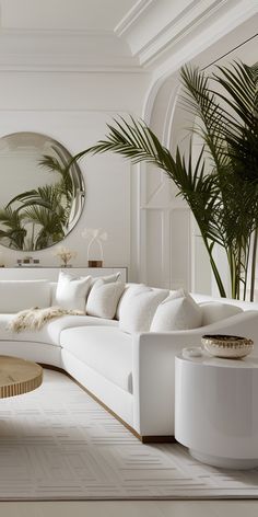 a living room with white couches and large mirrors on the wall above them, along with potted palm trees