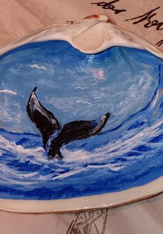 a blue and white plate with a black whale on it's side in the water