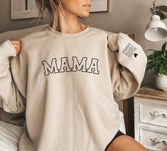 Personalized Mama Sweatshirt with Kid Names on Sleeve, Mothers Day Gift, Birthday Gift for Mom, New Mom Gift, Minimalist Cool Mom Sweater Ideal for any situation, a unisex heavy blend crewneck sweatshirt is pure comfort. These garments are made from polyester and cotton. This combination helps designs come out looking fresh and beautiful. The collar is ribbed knit, so it retains its shape even after washing.  Gildan 18000 Unisex Sweatshirt Materials: 50% cotton, 50% polyester Medium-heavy fabric Mama Sweater, Mama Hoodie, Teachers Gifts, Baby Swimsuit, Mom Sweater, Retro Baby, Vintage Mom, Mama Shirts, Personalized Gifts For Mom